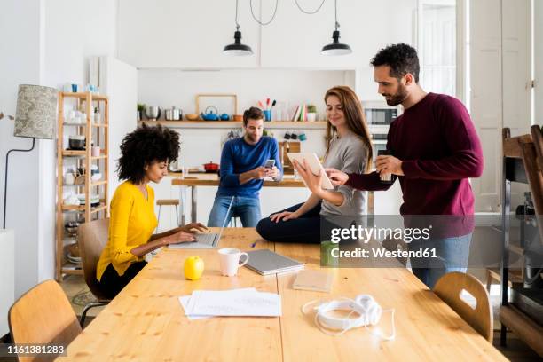 four friends in dining room at home with portable devices - shared living room stock pictures, royalty-free photos & images