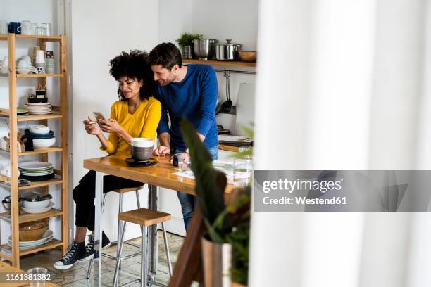 couple in kitchen at home sharing cell phone - couple kitchen stockfoto's en -beelden