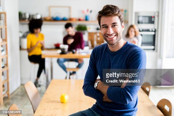 portrait of smiling man at dining table at home with friends in background - portrait of man smiling black jumper stock-fotos und bilder