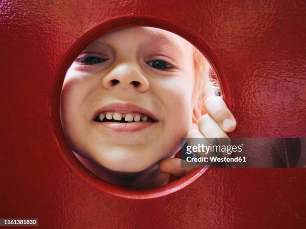 portrait of smiling little boy looking through hole on playground - peeking fotografías e imágenes de stock