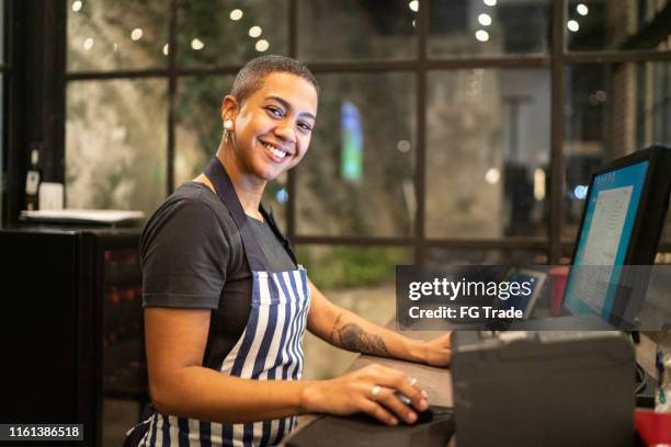 portrait of smiling cashier looking at camera and using computer - computer screen over shoulder stock pictures, royalty-free photos & images