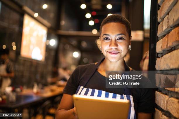 retrato da mulher nova que olha a câmera e que prende uma tabuleta digital no restaurante - pizzeria - fotografias e filmes do acervo