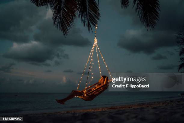 young adult woman relaxing on a swing in a tropical paradise - beach night stock pictures, royalty-free photos & images