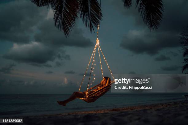 young adult woman relaxing on a swing in a tropical paradise - praia noite imagens e fotografias de stock