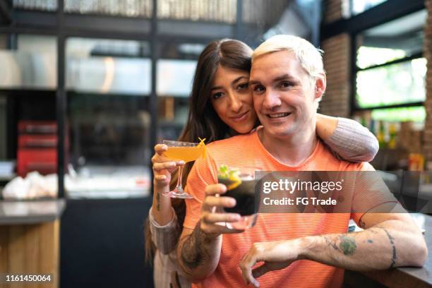 portrait of smiling friends looking at camera and holding drinks at restaurant - gay bar stock pictures, royalty-free photos & images