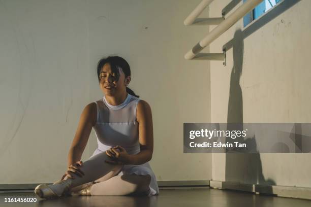 an asian chinese female teenager hurt her leg during practise in her ballet studio and sit on the floor with pain - ballet feet hurt stock pictures, royalty-free photos & images