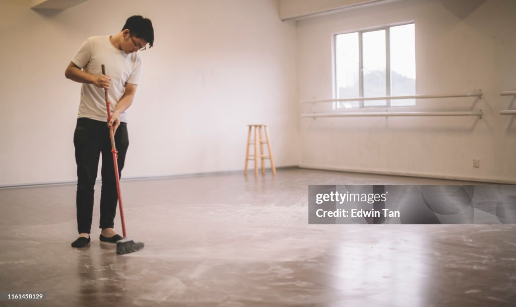 An asian chinese male dancer cleaning up ballet dancer floor sweeping after practise with broom