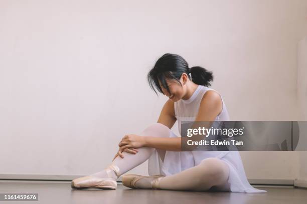 una adolescente asiática china se lastimó la pierna durante la práctica en su estudio de ballet y se sente en el suelo con dolor - leg show fotografías e imágenes de stock