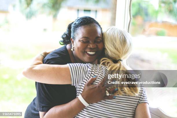 adult african american female e caucasica davanti alla porta di residenza salutarsi con un abbraccio - party social event foto e immagini stock