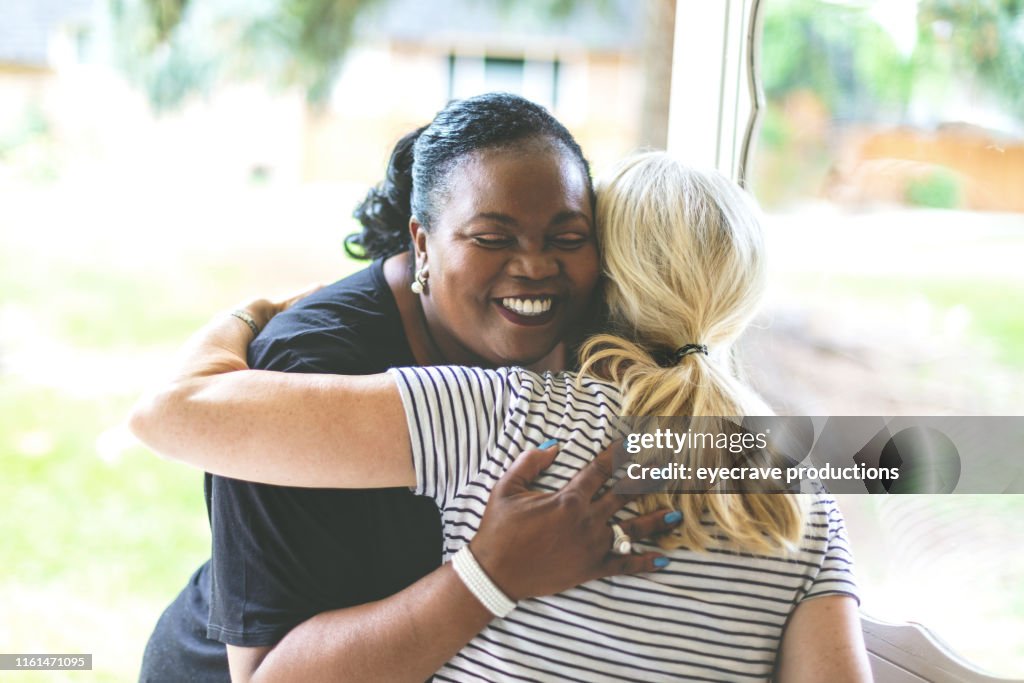 Adult African American Female and caucasian at front door of residence greeting each other with an embrace