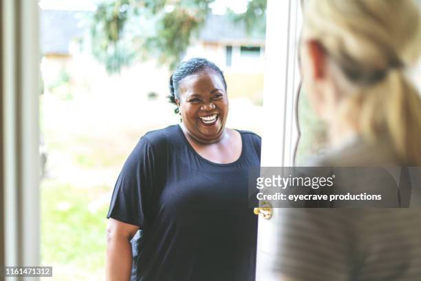 adult african american female and caucasian at front door of residence greeting each other - home visit stock pictures, royalty-free photos & images