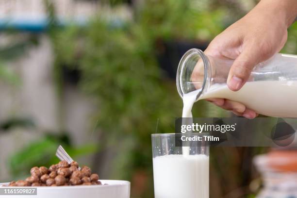 pouring milk in the cup of cereals with the green nature background. - milk pour - fotografias e filmes do acervo