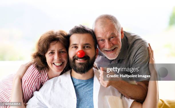 a portrait of senior couple with male doctor wearing red clown nose indoors. - funny clown stockfoto's en -beelden