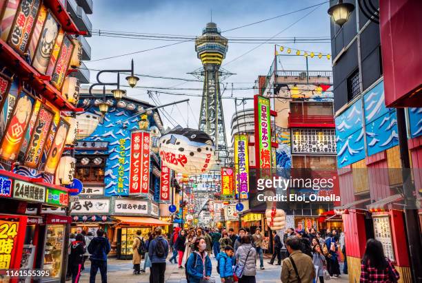 osaka tower and view of the neon advertisements in shinsekai district at dusk, osaka, japan - japan stock pictures, royalty-free photos & images