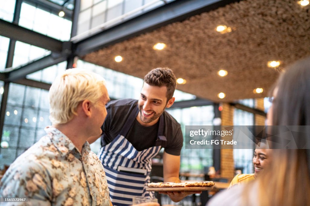 Waiter serving pizza to a group of friends