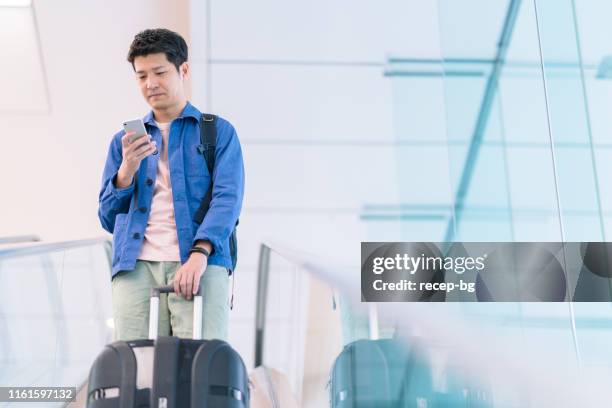 junge männliche tourist mit smartphone, während er sein gepäck hält - male airport stock-fotos und bilder