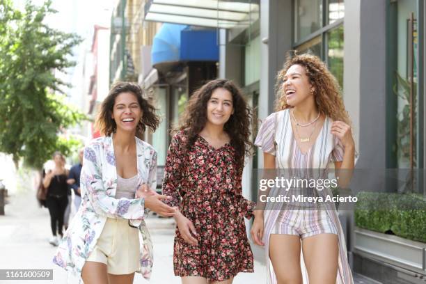 three female latinx millennials laugh while walking outdoors on a warm summer day in new york city. - veste à motif floral photos et images de collection