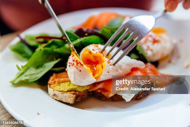 cutting poached egg on top of avocado toast with salmon - proteina foto e immagini stock