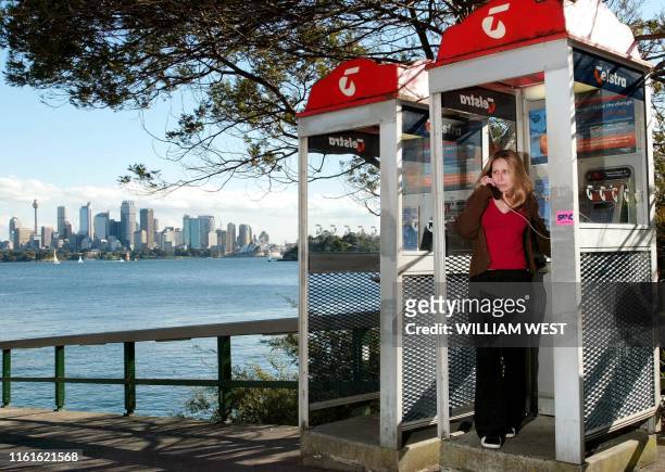 Roberta Alvim uses a Telstra payphone at the Taronga Zoo wharf as the skyline of Sydney looms in the background, 28 August 2002. Telstra Corp,...