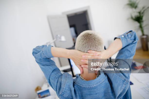 Berlin, Germany Symbolic photo on the topic of break in the office: A woman is sitting at the desk and keep her arms behind her head on August 14,...