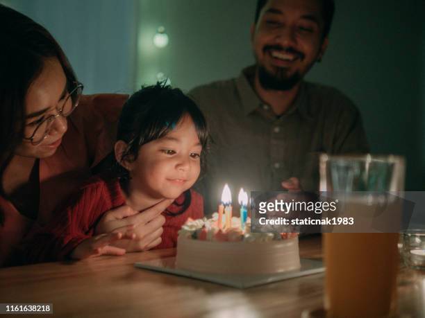 bambino che festeggia la sua festa di compleanno a casa - parents children blow candles asians foto e immagini stock
