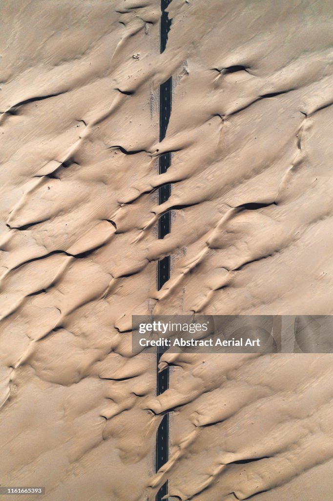 Abstract patterns crossing a desert road taken by drone, United Arab Emirates