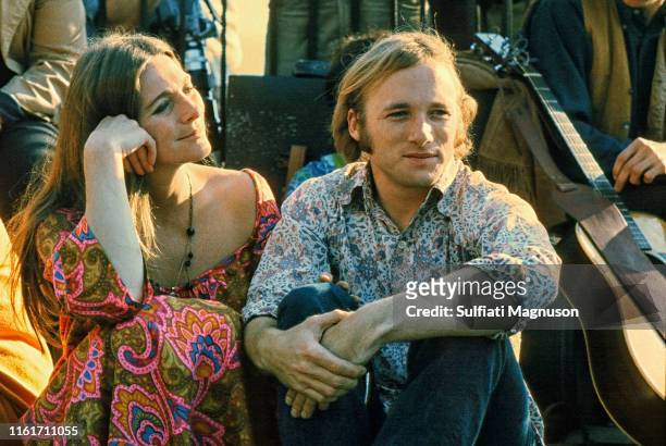 Judy Collins, in profile with head on right hand, entwined with Stephen Stills in a blue and white shirt, with late afternoon sun casting shadows,...