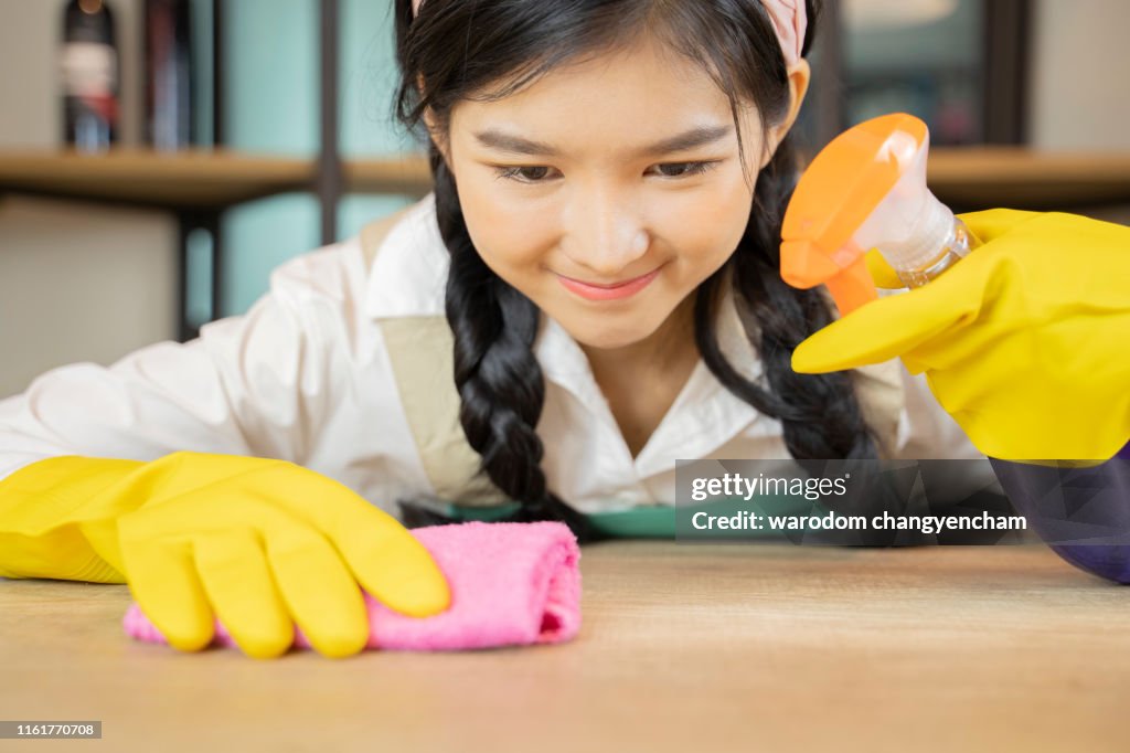 Woman cleaning kitchen tabel with sponge and spray cleaner.