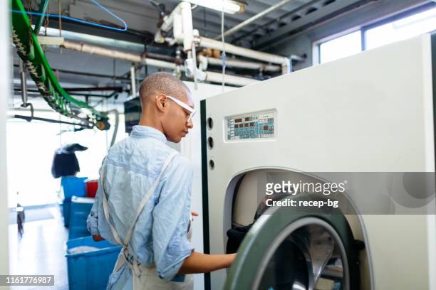 jeune femme mettant des vêtements dans la machine sèche de nettoyage - dry cleaning photos et images de collection