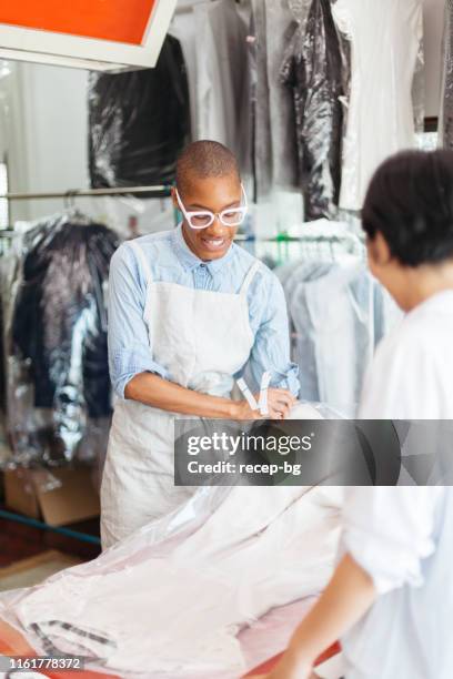 young woman working at dry cleaning shop and talking to costumer - dry cleaners stock pictures, royalty-free photos & images