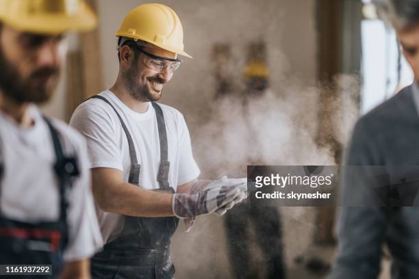 trabajador de la construcción feliz de la limpieza de sus guantes de aserrín en el apartamento renovador. - built structure fotografías e imágenes de stock