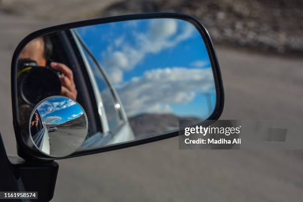 a man taking a selfie in side view mirror of a car during an outdoor adventure with clouds and sky also visible - convex stock pictures, royalty-free photos & images