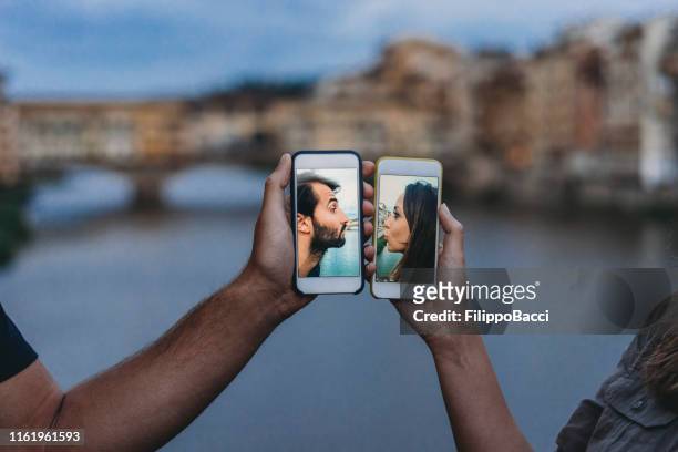 konzeptaufnahme eines jungen erwachsenen paares, das sich per handy küsst - dating stock-fotos und bilder