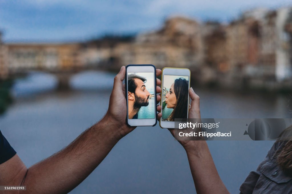 Conceptuele shot van een jong volwassen paar zoenen via mobiele telefoon