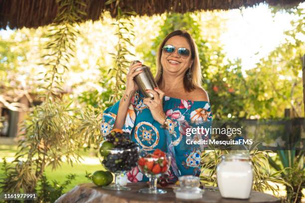 mujer madura preparando cóctel con coctelera - cocktail making fotografías e imágenes de stock