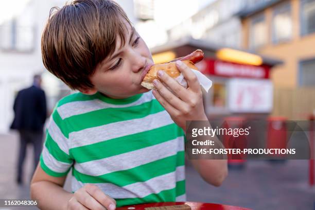 cute boy is eating fast food - hot dog - hot dog schnellimbiss stock-fotos und bilder