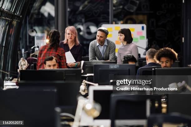 group of people talking around desk in busy office - crowded-office-desk stock pictures, royalty-free photos & images