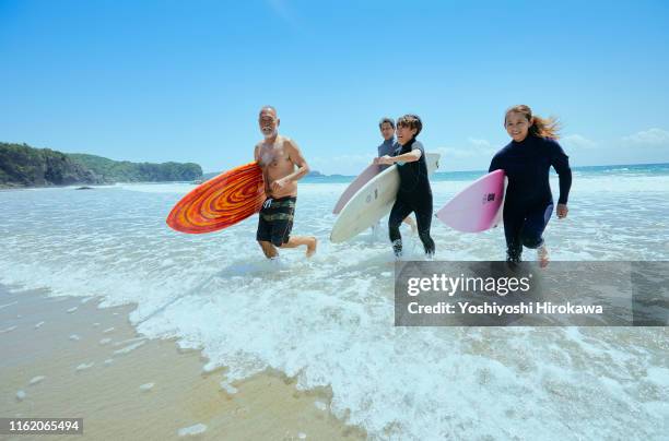 senior surfers running towards beach from sea - shizuoka prefecture stock pictures, royalty-free photos & images