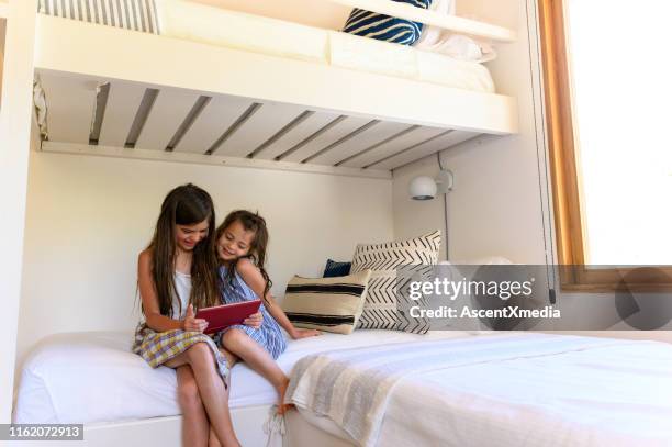 hermanas usando una tableta digital mientras están sentadas en la cama - litera fotografías e imágenes de stock