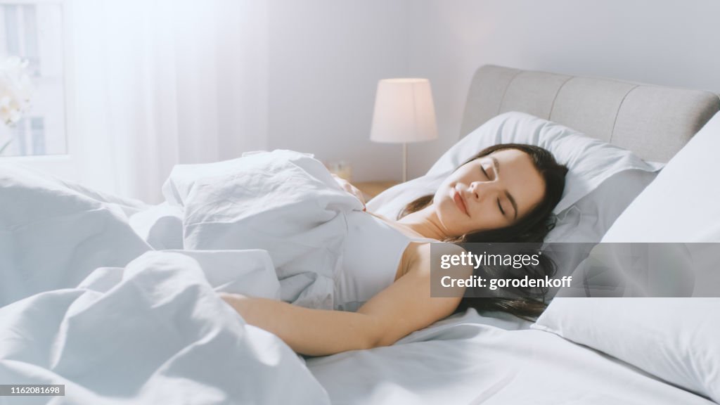 Atraente morena cozily dorme em sua cama enquanto sunrays amanhecer iluminá-la. Retrato morno, acolhedor e doce do sono da beleza