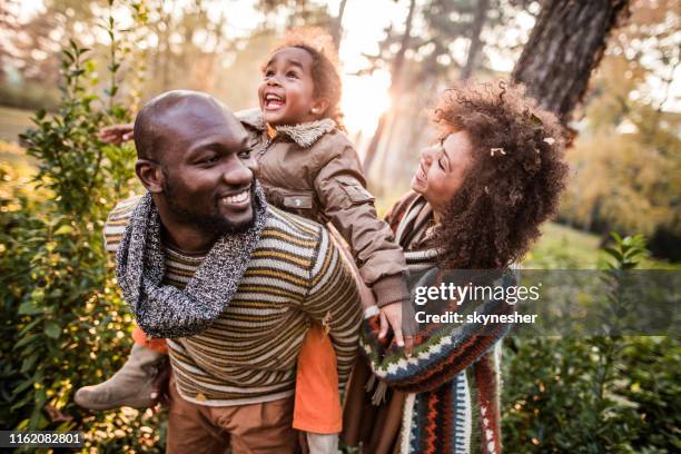 happy black parents having fun with their daughter at the park. - park couple piggyback stock pictures, royalty-free photos & images