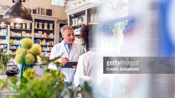 reife männliche und junge apothekerin arbeiten zusammen - homeopathic medicine stock-fotos und bilder
