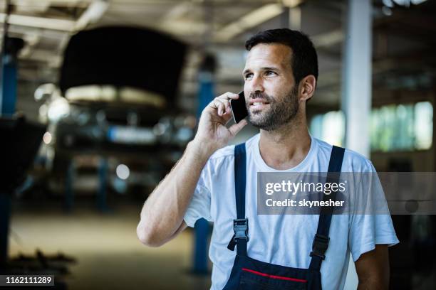 glücklicher automechaniker, der in einer werkstatt auf dem handy spricht. - fachmann auto smartphone stock-fotos und bilder