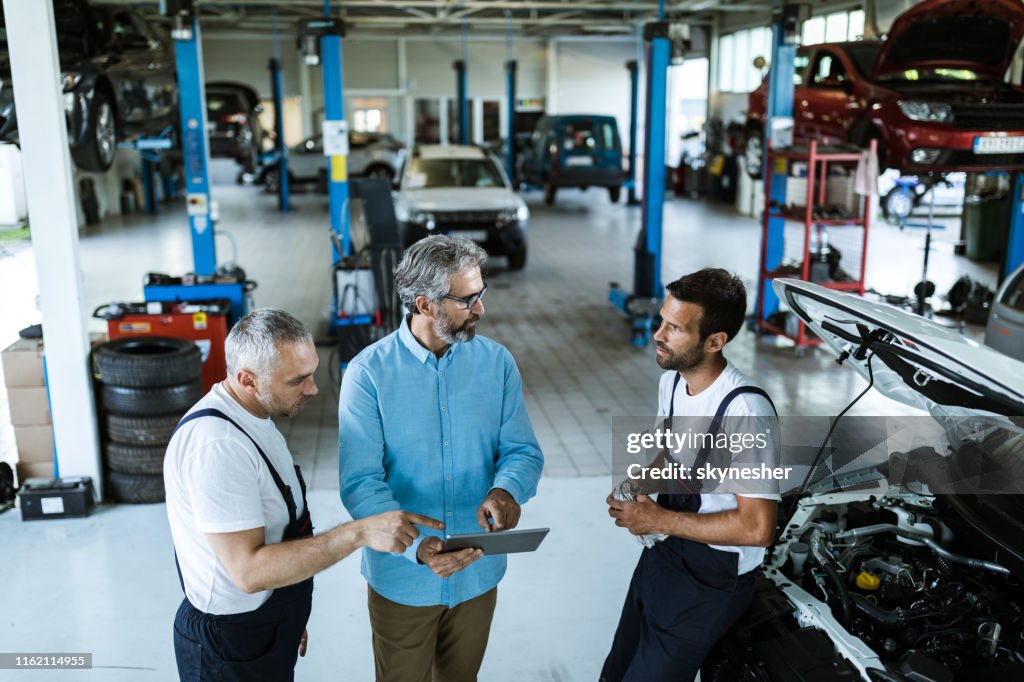 Gerente de adultos medio usando touchpad y hablando con mecánicos de coches en un taller.