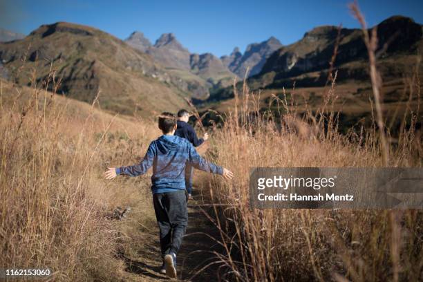 rearview of boy and his father  hiking along a mountain path - drakensberg stock pictures, royalty-free photos & images