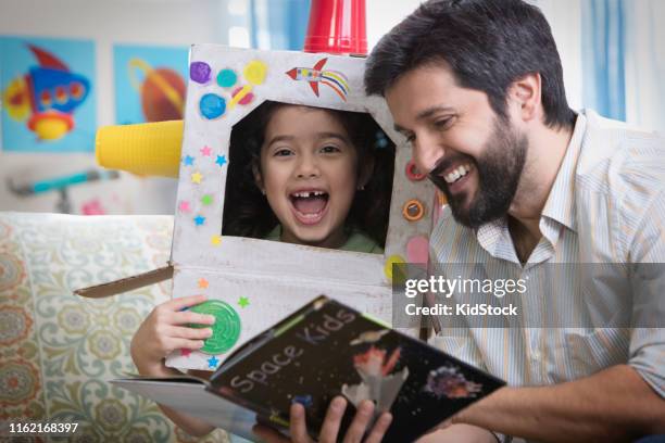 father and daughter reading a book sitting on sofa - kidstock girl stock pictures, royalty-free photos & images