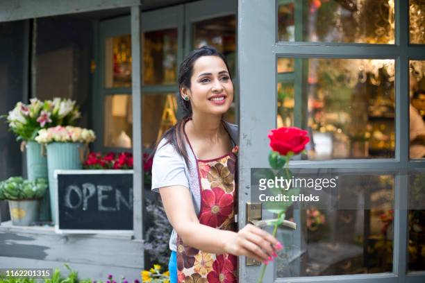 female florist with red rose in flower shop doorway - beautiful woman stock pictures, royalty-free photos & images