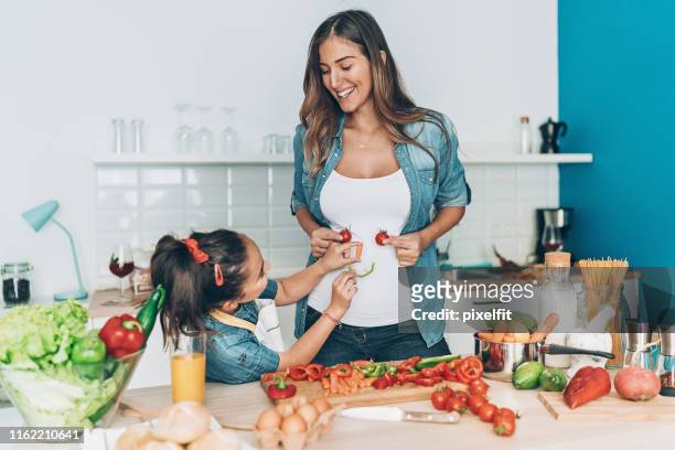 pregnant mother and daughter making vegetable smiley face - stomach stock pictures, royalty-free photos & images