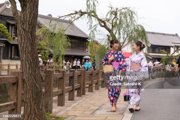 junge freundinnen in yukata zu fuß in traditionellen japanischen dorf - yukata kimono stock-fotos und bilder