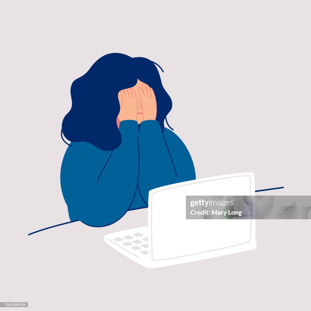 Entstellte Frau sitzt am Computer und weint ihr Gesicht mit ihren Händen.